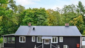 Une maison noire avec un toit gris, des fenêtres blanches et un petit porche.