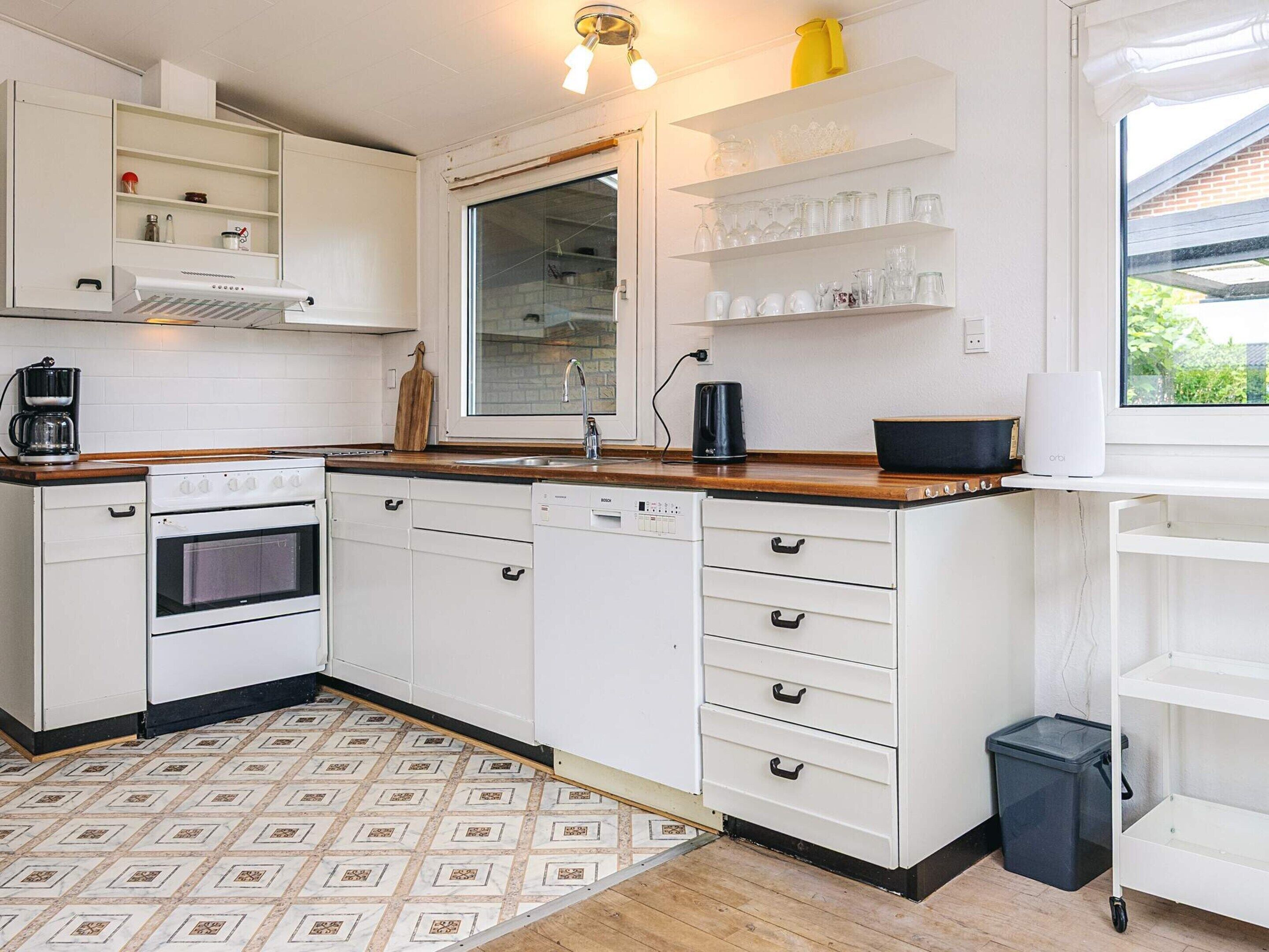 A modern kitchen with white cabinetry, a built-in oven, a dishwasher, and a window with a view of greenery outside.