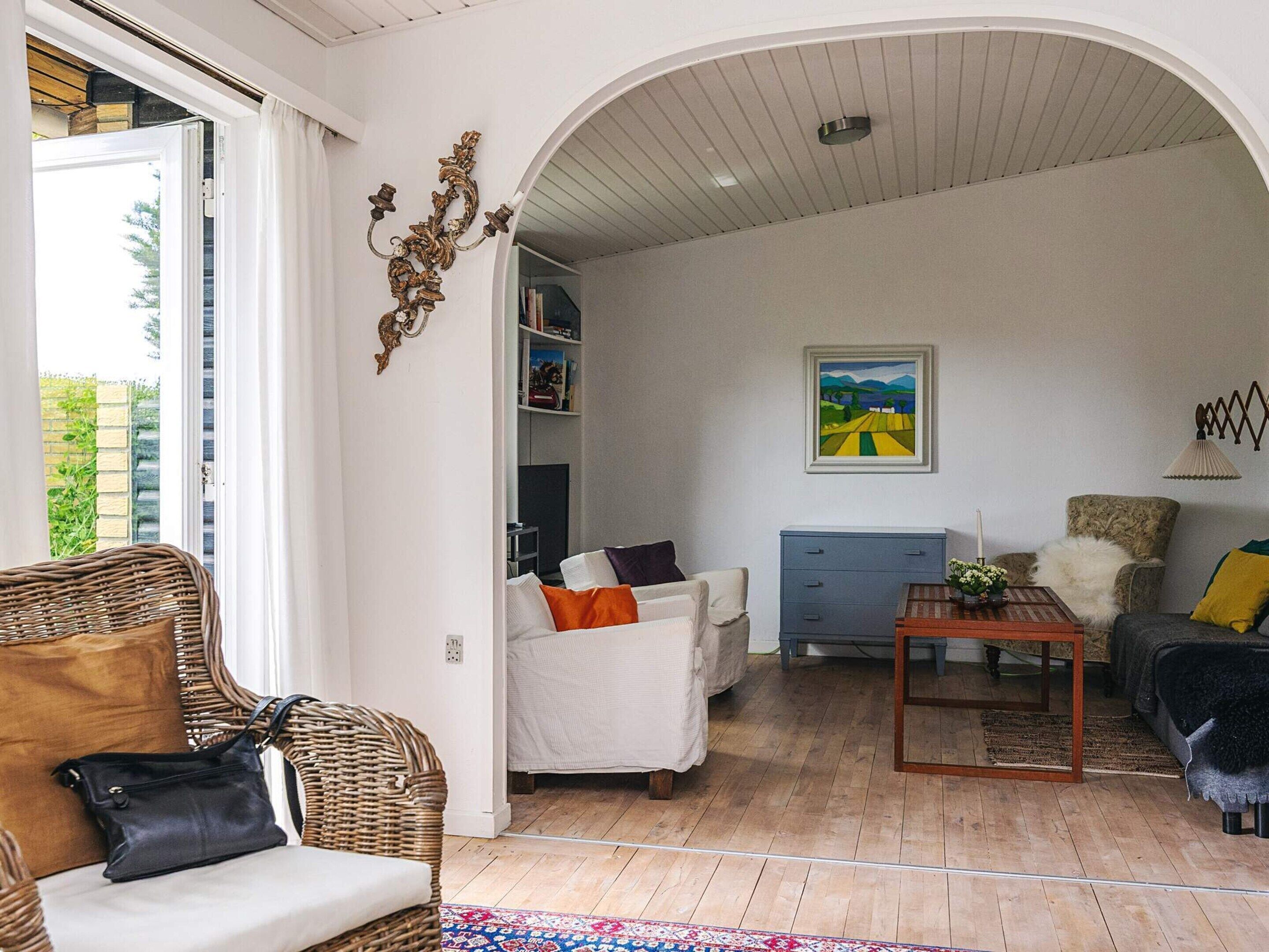 A living room with a wicker chair, a white sofa, a blue cabinet, and a painting on the wall.