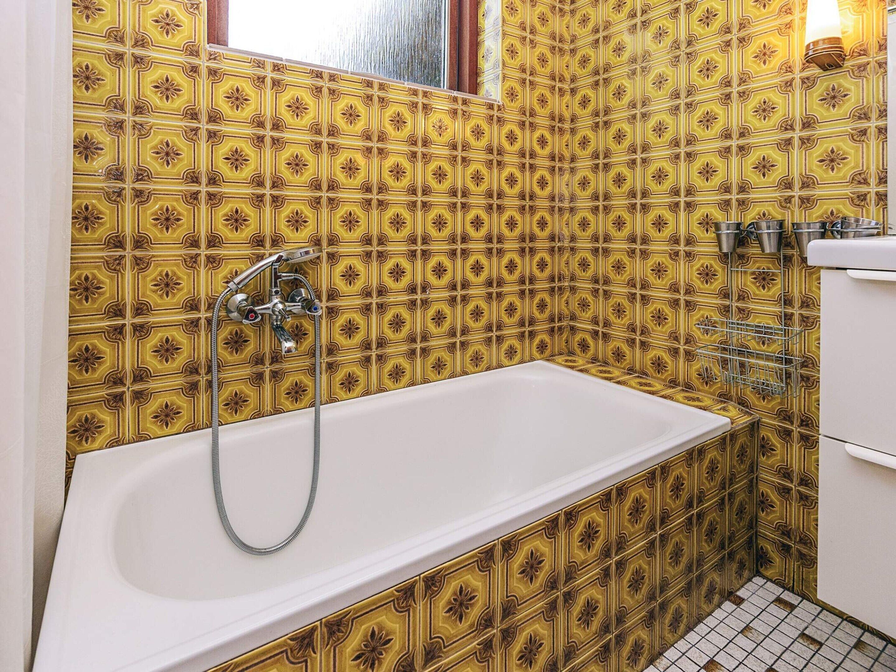 A bathroom with a white bathtub, yellow patterned tiles, and a window.