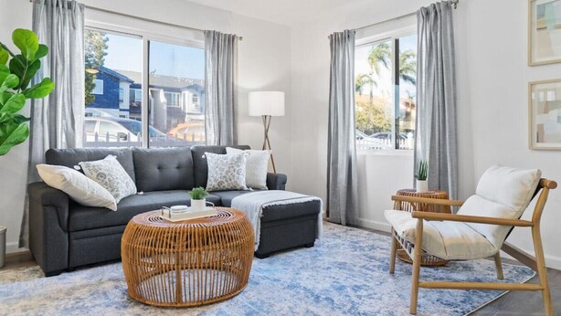 A modern living room with a grey sofa, a round wicker coffee table, a white armchair, and a blue patterned rug. - Coastal 2BR Escape with High-Speed WiFi (San Diego)