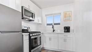 A modern kitchen with white cabinetry, a stainless steel refrigerator, a microwave, a stove, and a coffee maker. - Coastal 2BR Escape with High-Speed WiFi (San Diego)
