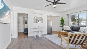 A spacious living area with a modern ceiling fan, a dining table, a sofa, and a large window offering a view of the outside. - Coastal 2BR Escape with High-Speed WiFi (San Diego)