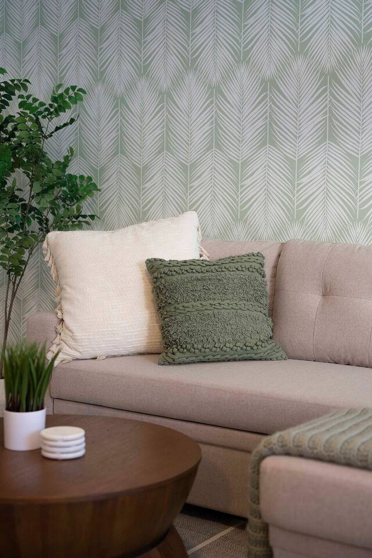 A beige sofa with two pillows, a round wooden coffee table, and a potted plant.