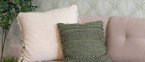 A beige sofa with two pillows, a round wooden coffee table, and a potted plant.