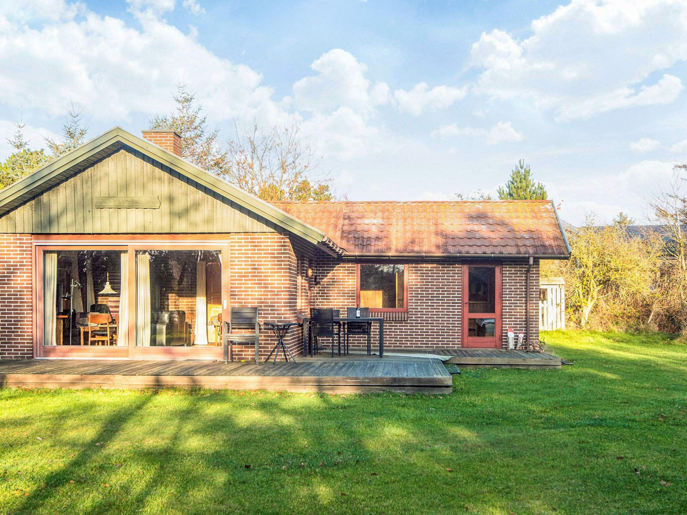 A single-story brick house with a large sliding glass door entrance, a covered patio with outdoor furniture, and a well-maintained lawn.