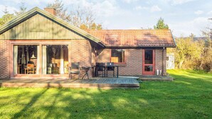 A single-story brick house with a large sliding glass door entrance, a covered patio with outdoor furniture, and a well-maintained lawn.