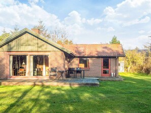 A single-story brick house with a large sliding glass door entrance, a covered patio with outdoor furniture, and a well-maintained lawn.