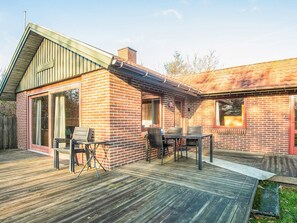 A brick house with a wooden deck, a covered patio, and a dining area with outdoor furniture. - 4 Person Holiday Home in Blavand (Blavand)