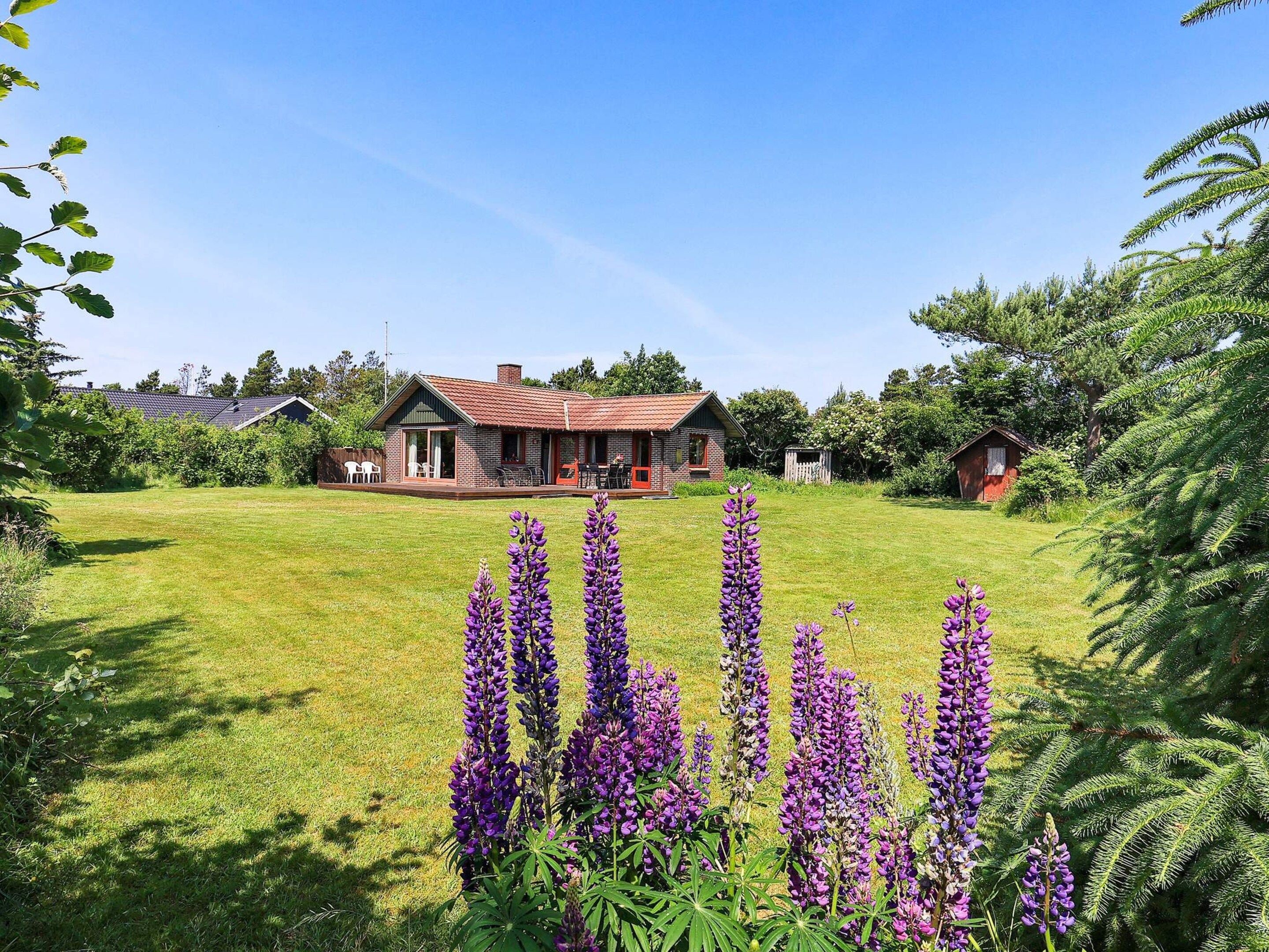 A house with a red roof, a porch, and a lawn with purple flowers.