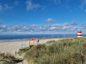 A beach with a red and white striped lighthouse, grassy dunes, and informational signs. - 4 Person Holiday Home in Blavand (Blavand)