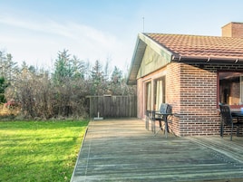 Un jardin avec une terrasse en bois, une maison en briques et une clôture en bois.