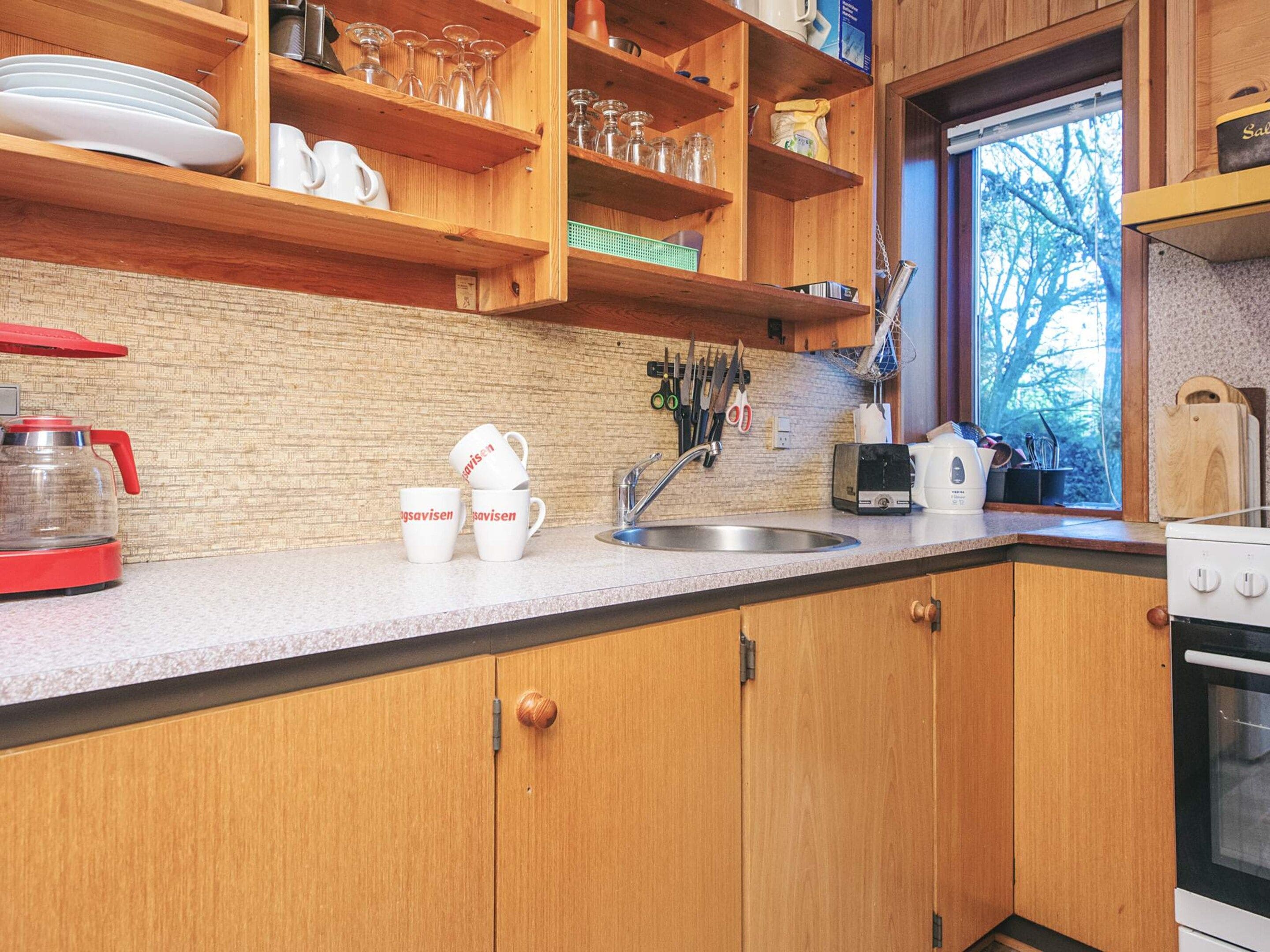 A kitchen with wooden cabinets, a stainless steel sink, and a window with a view of trees.