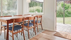 A dining area with a wooden table and chairs, large windows, and a view of greenery outside. - 6 Person Holiday Home in Allinge (Allinge)