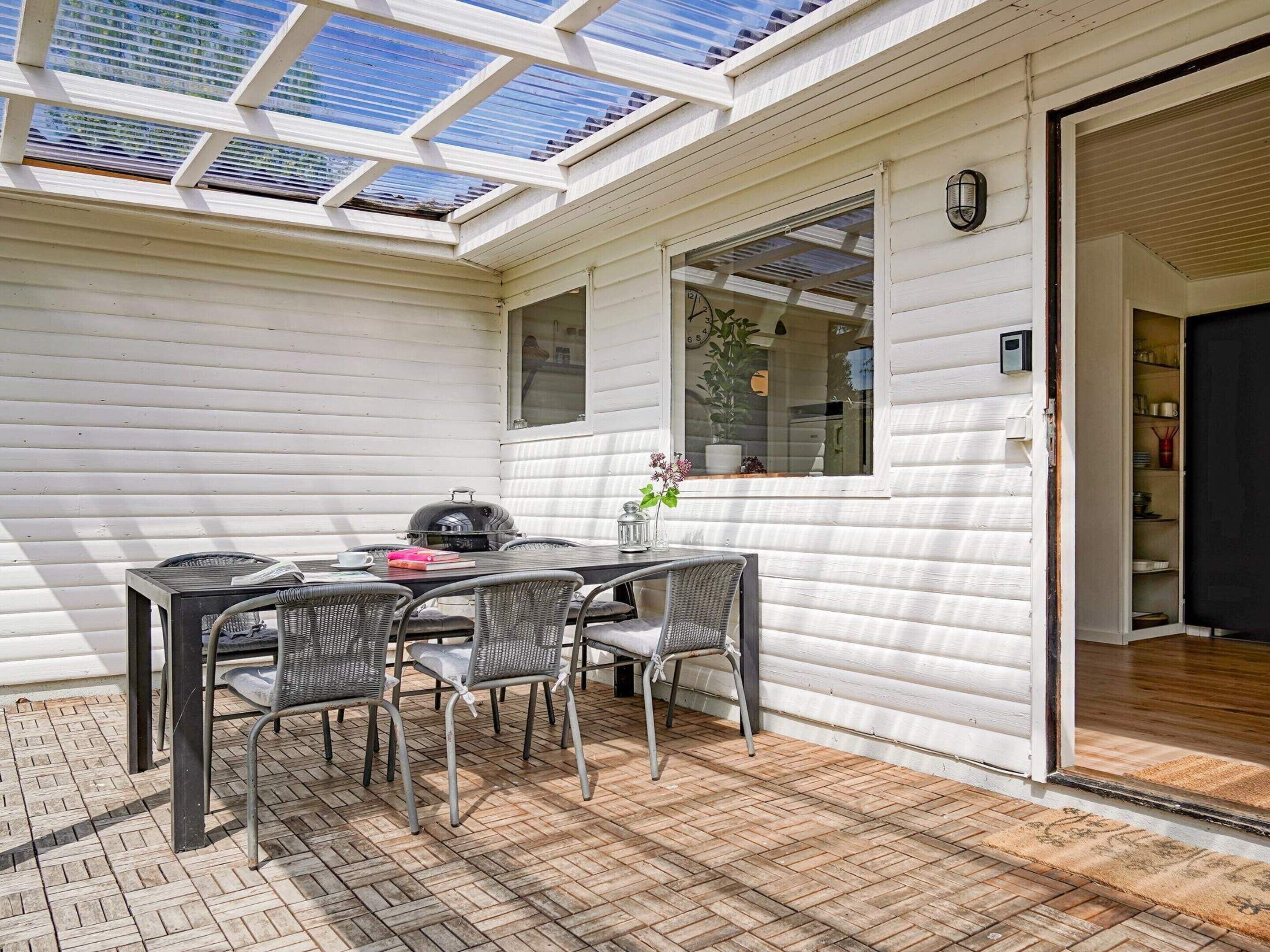 A covered patio with a table and chairs, a grill, and a window with a view of the sky.