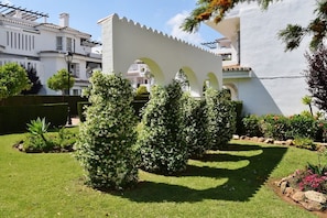A white building with a modern design, featuring a unique white archway and a well-maintained garden with various shrubs and flowers.