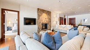 A modern living room with a stone fireplace, a flat-screen TV, and a large beige sofa with blue cushions. - Solaris Residences 5C West (Vail)