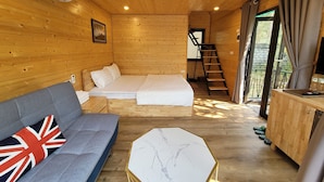 A cozy cabin interior with a sofa, a bed, a desk, and a staircase leading to a balcony. - Truc An Village (Xuan Hoa)