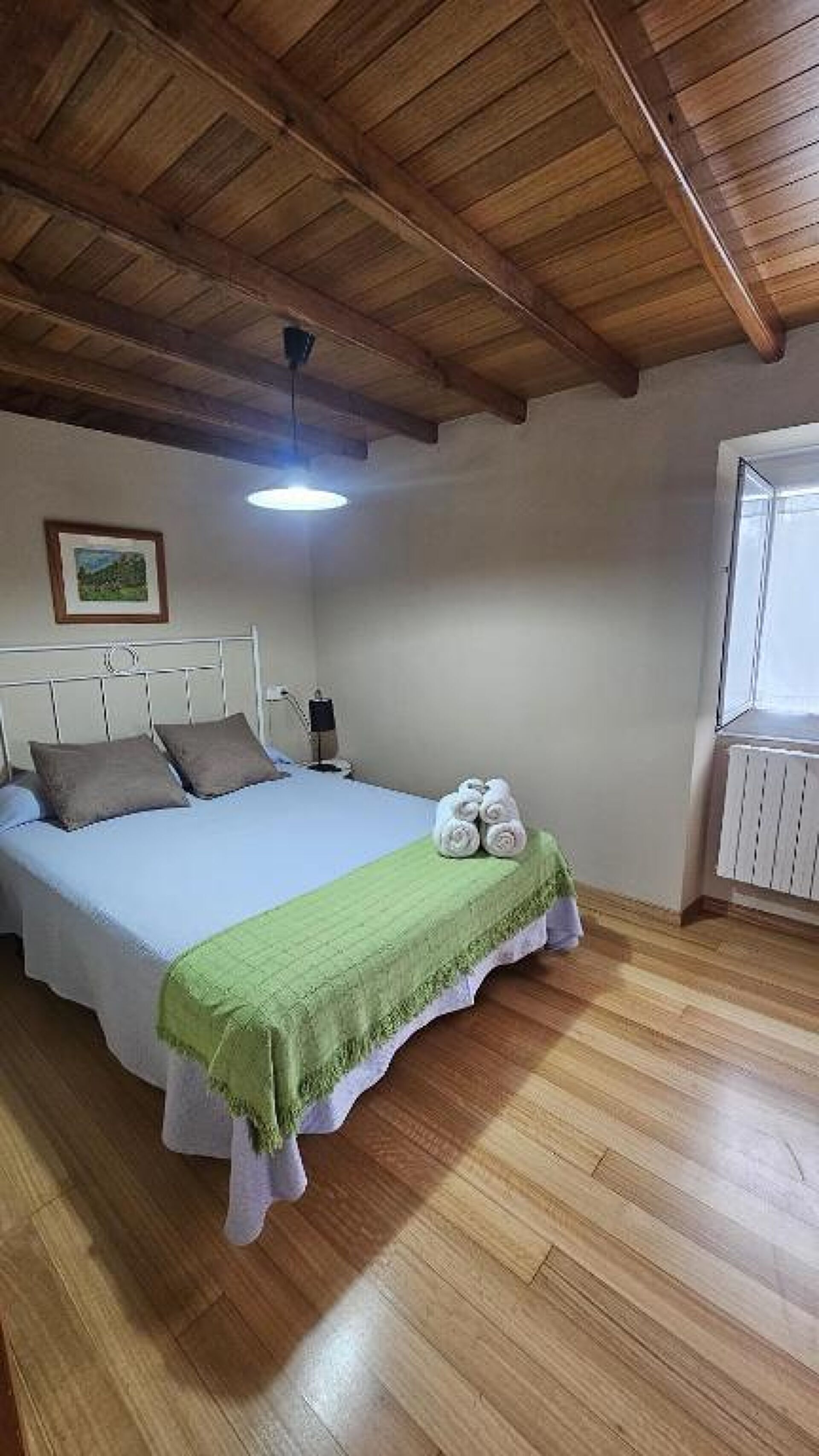 A bedroom with a bed, a green throw blanket, and a window.