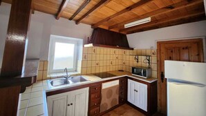 A kitchen with wooden beams, a window, a sink, cabinets, a microwave, and a refrigerator. - La Casita del Pueblo (Coaña)