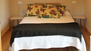 A bedroom with a wooden ceiling, a bed with a floral pillow, two bedside tables, and a hanging light fixture. - La Casita del Pueblo (Coaña)