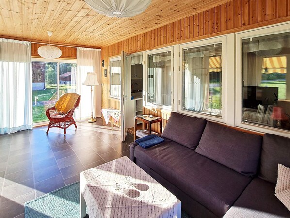 A modern living room with a sofa, a chair, and a table. There are large windows and a door leading to a balcony.