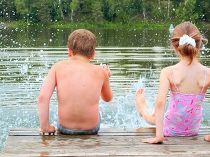 Two children sitting on a wooden dock by a body of water. - 4 Star Holiday Home in Ljusdal (Ljusdal)