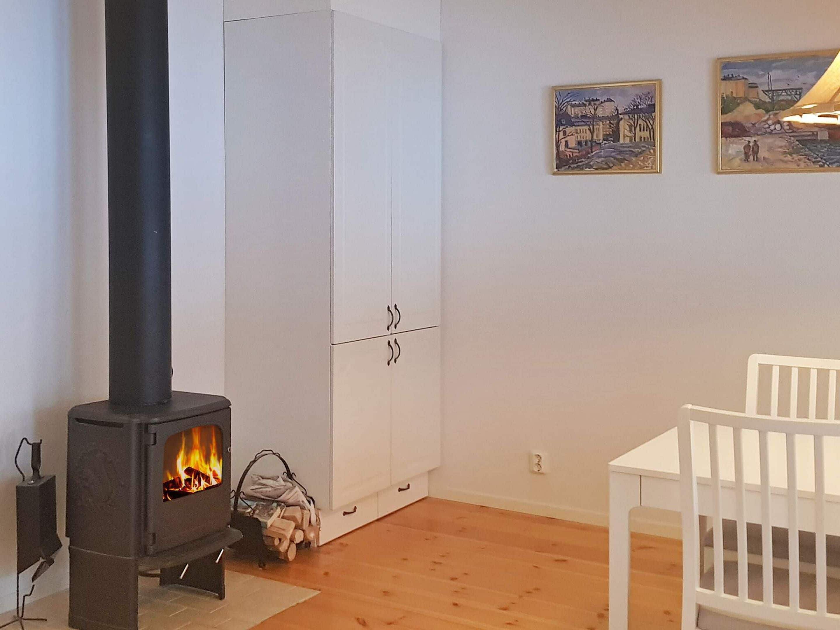 A room with a wood-burning stove, a white wardrobe, and a white chair.