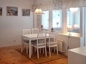 A dining area with a white table and chairs, a window with curtains, and a lamp on the windowsill. - 4 Star Holiday Home in Ljusdal (Ljusdal)