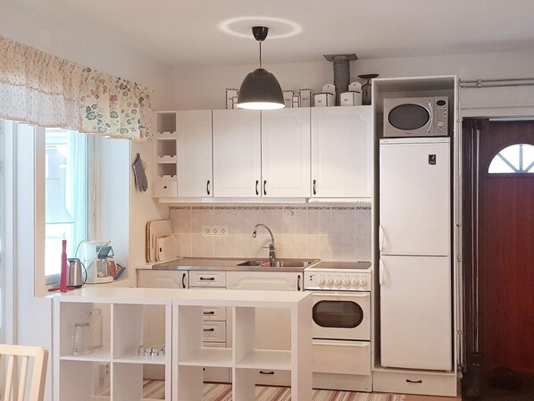 Una cucina compatta con mobili bianchi, forno integrato e microonde.
