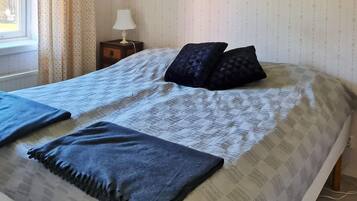 A neatly made bed with a patterned bedspread and two pillows, a bedside table with a lamp, and a window with curtains.