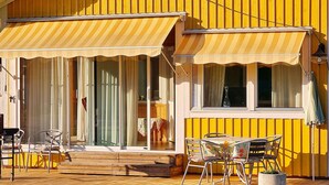 A yellow building with a covered patio area, a table with chairs, and a sliding glass door. - 4 Star Holiday Home in Ljusdal (Ljusdal)