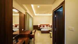 A hotel room with a wooden desk, a bed with a headboard, a mirror, and a ceiling fan. - Zip By Spree Hotels Purple Orchid Whitefield (Bengaluru)