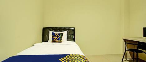 A single bed with a headboard, a desk with a chair, and a computer monitor.