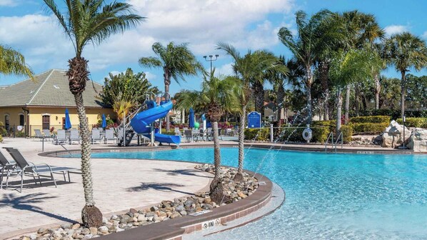 A swimming pool with a water slide, lounge chairs, palm trees, and a building with a tiled roof. - Rent the Perfect 4 Bedroom Townhome on Paradise Palms Resort, Orlando Townhome 6145 (Kissimmee)