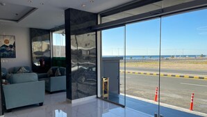 A modern lobby with a glass wall offering a view of the road and beach. - Sweet Land Hotel (Umluj)