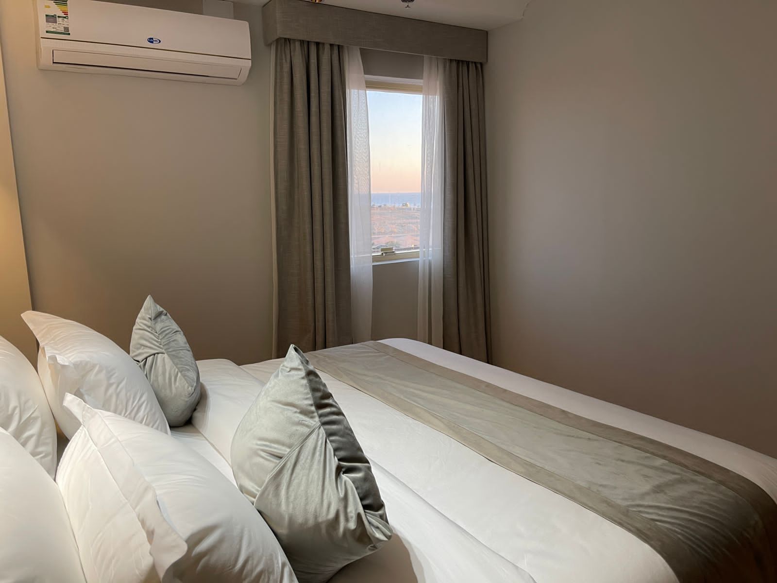 Una habitación de hotel con cama, almohadas, ventana con cortinas y aire acondicionado.