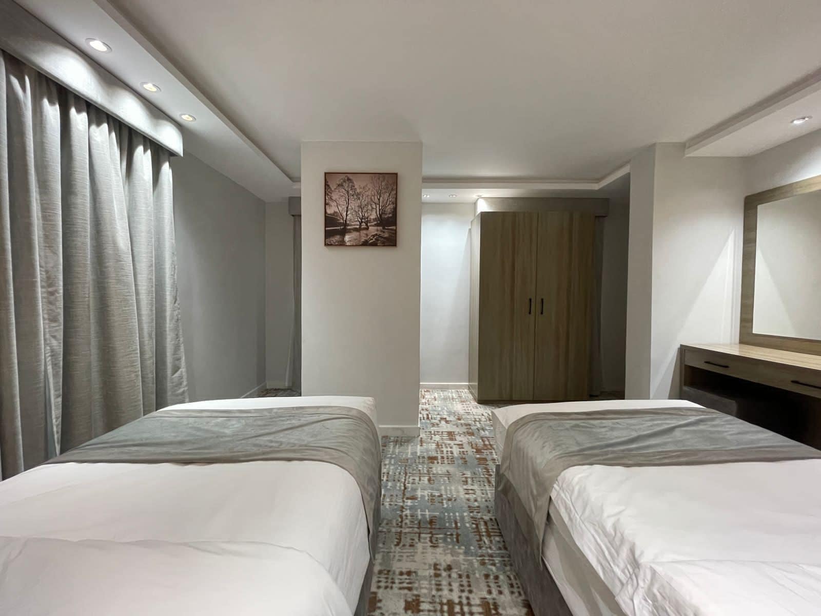 Una habitación de hotel con dos camas, un armario, un espejo y un cuadro en la pared.