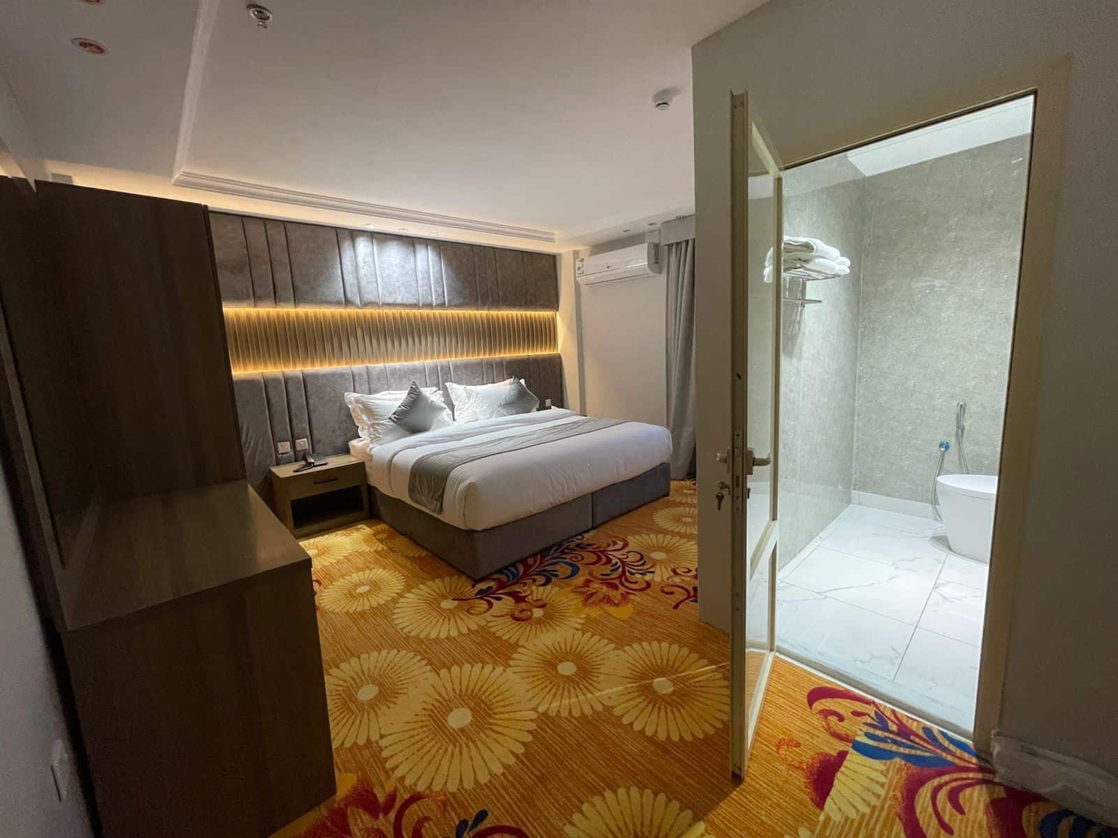 Una habitación de hotel moderna con una cama grande, ducha a ras de suelo y alfombra estampada.