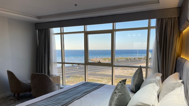 A hotel room with a large bed, a view of the beach, and a chair. - Sweet Land Hotel (Umluj)