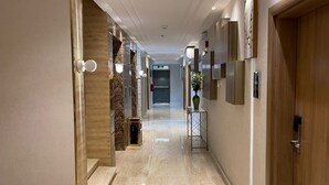 A modern hotel corridor with marble flooring, wooden accents, and wall-mounted lighting. - Sweet Land Hotel (Umluj)
