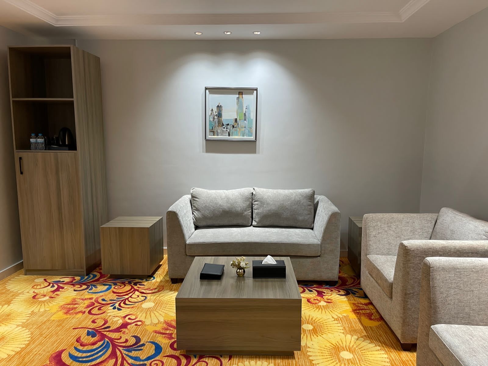 Un salon moderne avec un canapé gris, un fauteuil assorti, une table basse en bois et un tapis aux motifs colorés.