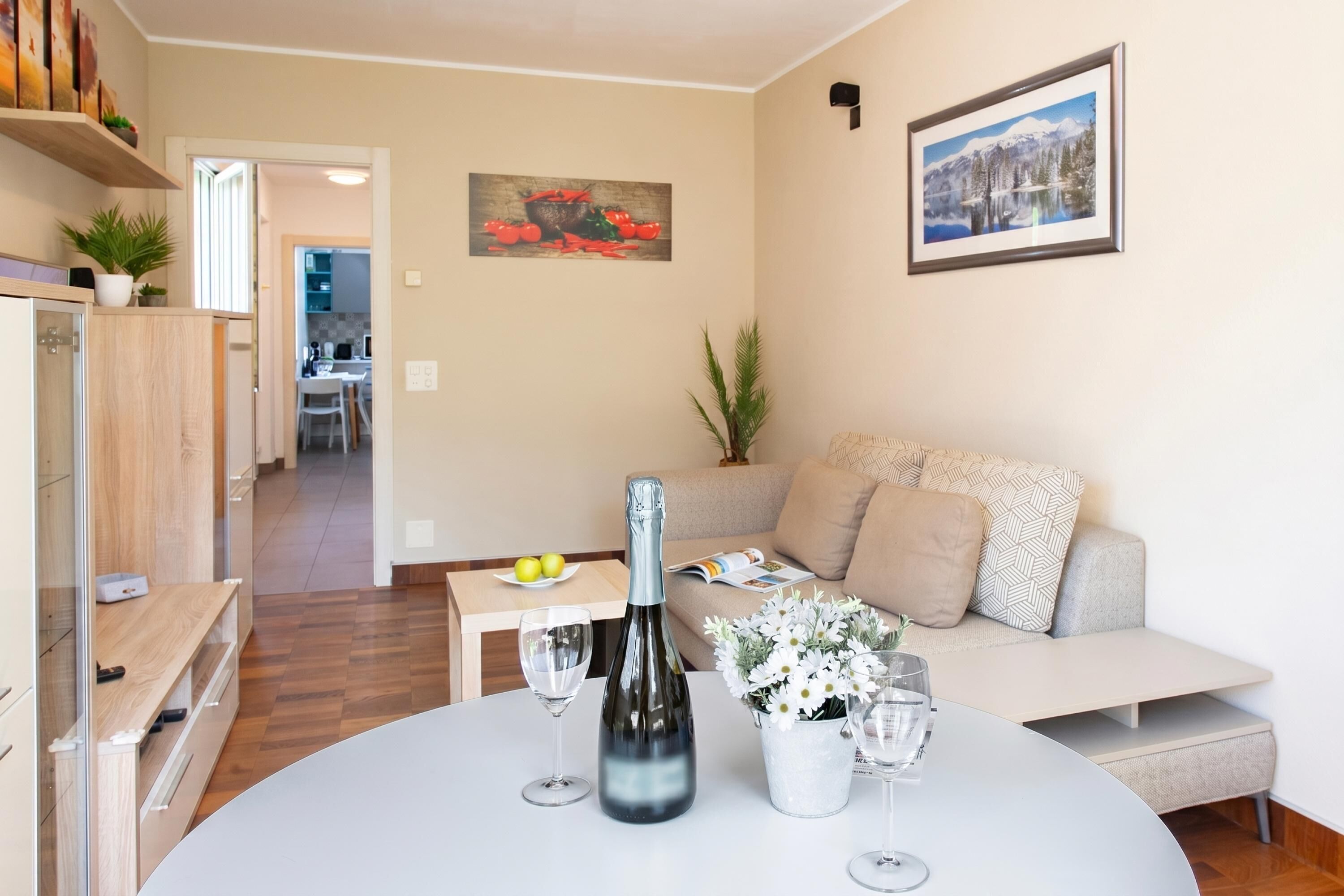 Een moderne woonkamer met een ronde tafel, een bank, een eethoek op de achtergrond en een keuken die door een open deur zichtbaar is.