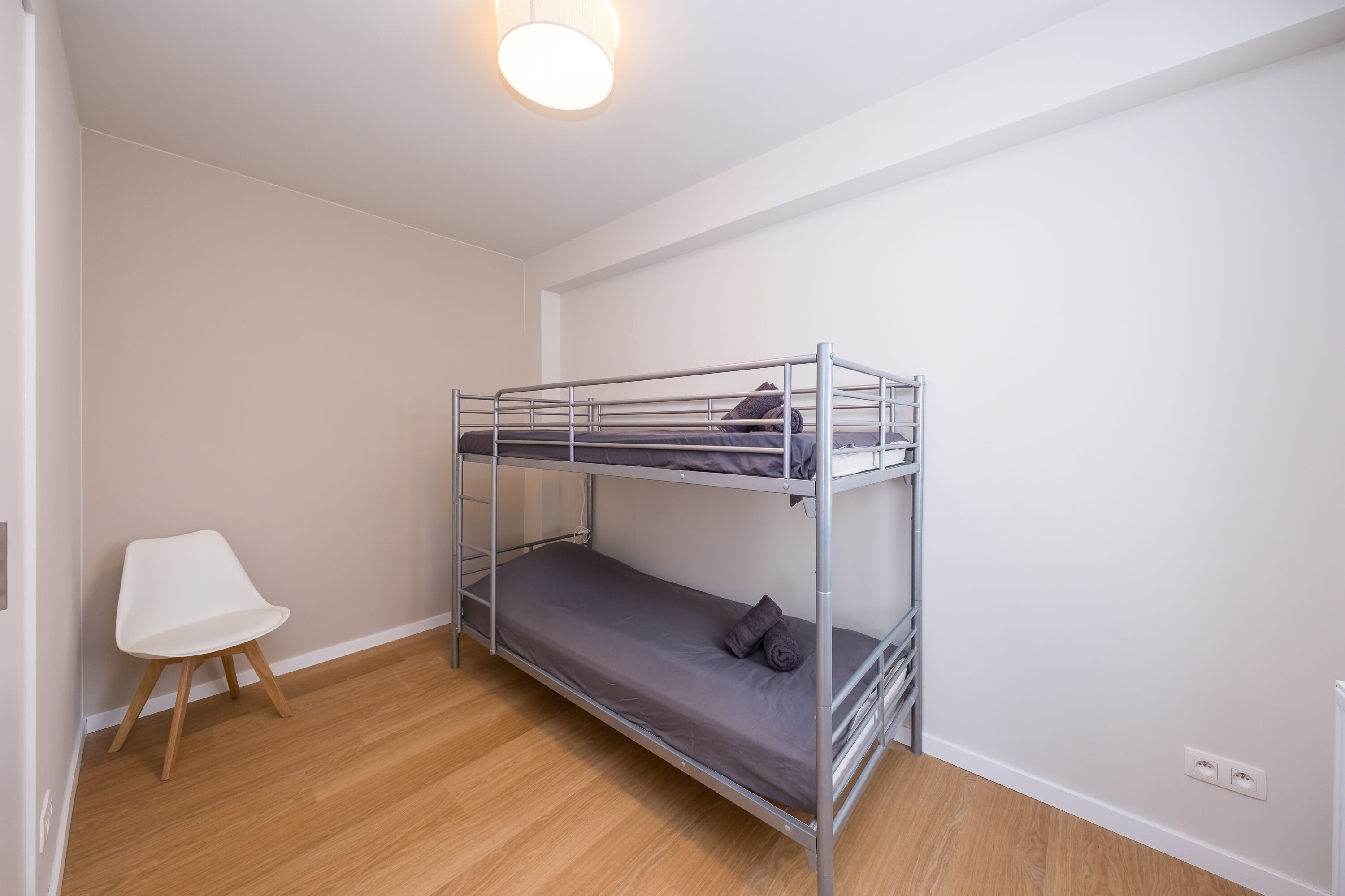 A bunk bed room with a white chair and a wooden floor.