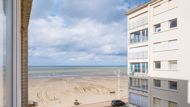 A view from a window overlooking a beach with a building in the foreground. - Seashore (Koksijde)