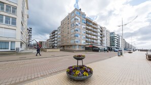 A multi-story building with balconies, a paved walkway, and a flower bed in the foreground. - Seashore (Koksijde)