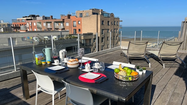 Terraza en la azotea con una mesa lista para comer, con vistas a una playa y edificios.