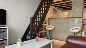 A modern living room with a white table, red leather sofa, a TV, and a staircase with a wooden railing. - 3-room apartment for 4 in Châtelaillon-Plage with parking (Châtelaillon-Plage)