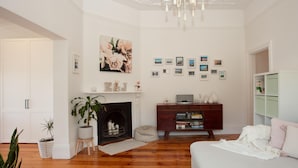 A well-lit living room with a fireplace, a bookshelf, and a large floral painting on the wall.