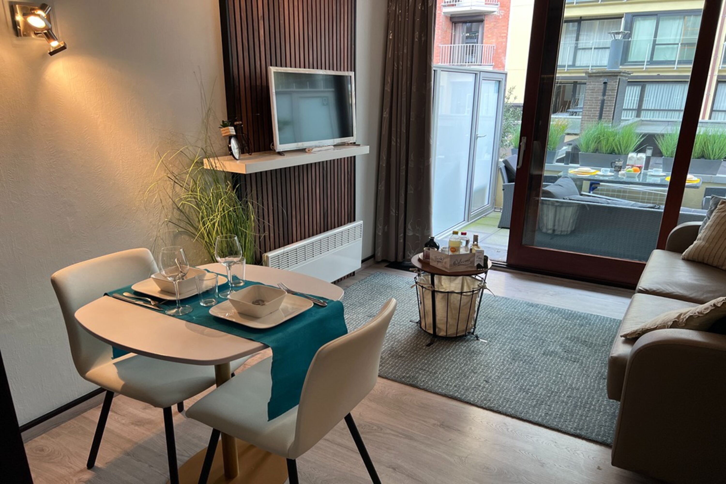 Un comedor con una mesa preparada para dos, un televisor en un estante y vistas al balcón.